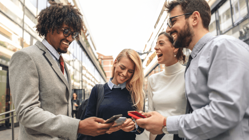 Image of a group of people talking, smiling, and laughing, while looking at their smartphones.